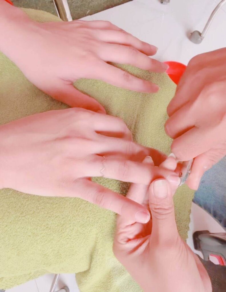 Nail technician carefully using nippers to prep a client's cuticles over a green towel.