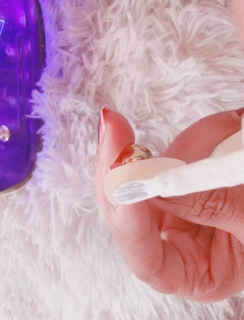 Painting a smooth, thin layer of white gel polish onto a practice tip using the polish brush.