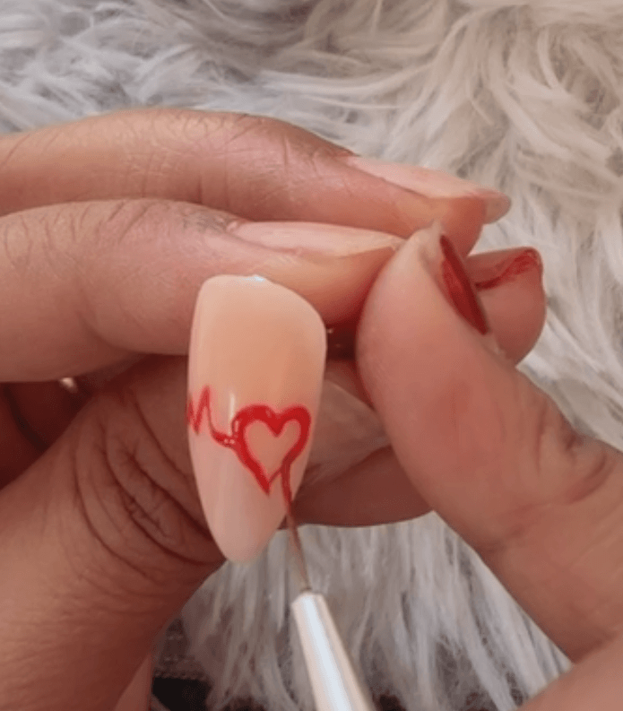 Detailed view of the fine white liner brush refining the bottom point of the red heart outline, connecting it smoothly back to the EKG wave line.