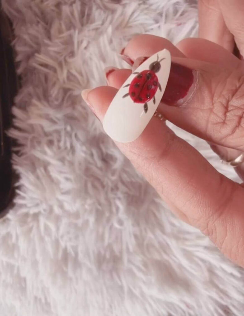 Close up of a completed ladybug nail art design featuring a red body, black spots, and tiny antennae.