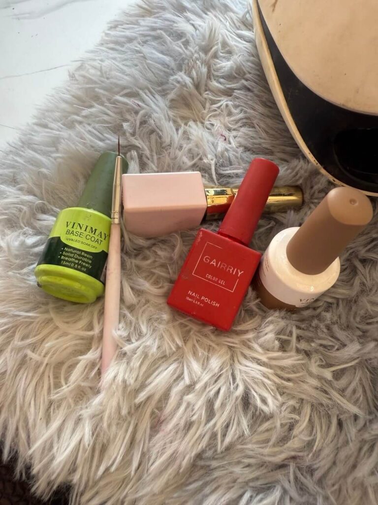 Nail technician tools laid out on a fluffy white rug, including Vinimay Base Coat, Gairriy Red Color Gel, a fine liner brush, and a UV LED nail lamp.