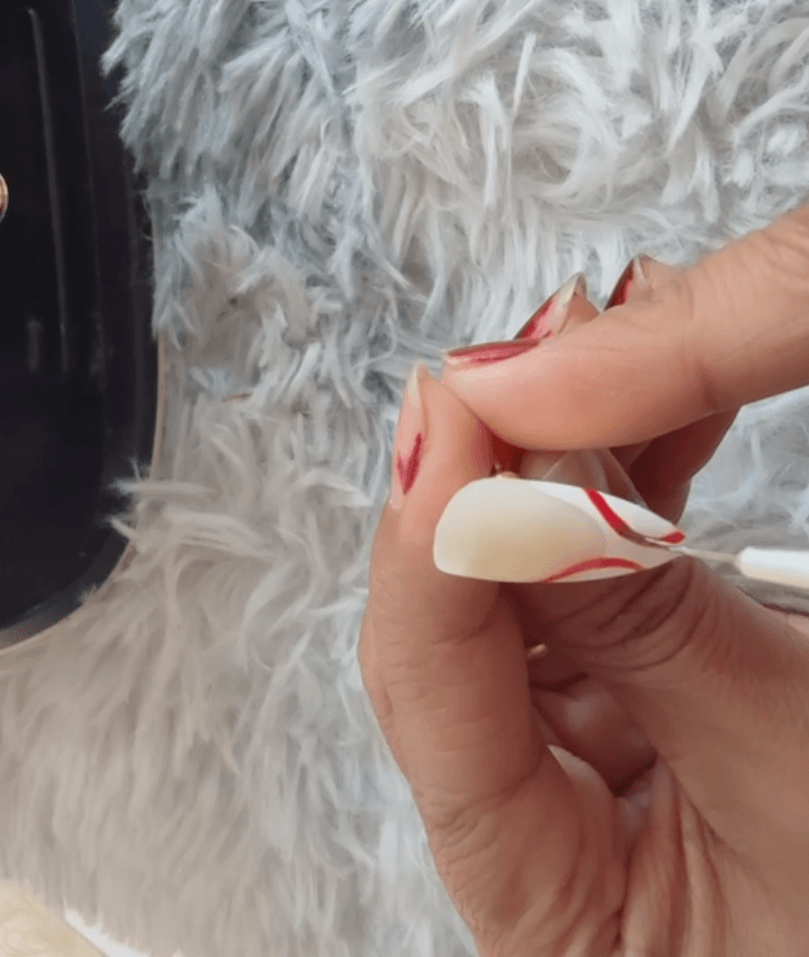 Using a fine tool to apply a small red design detail over a white base coat for a minimalist nail art look.