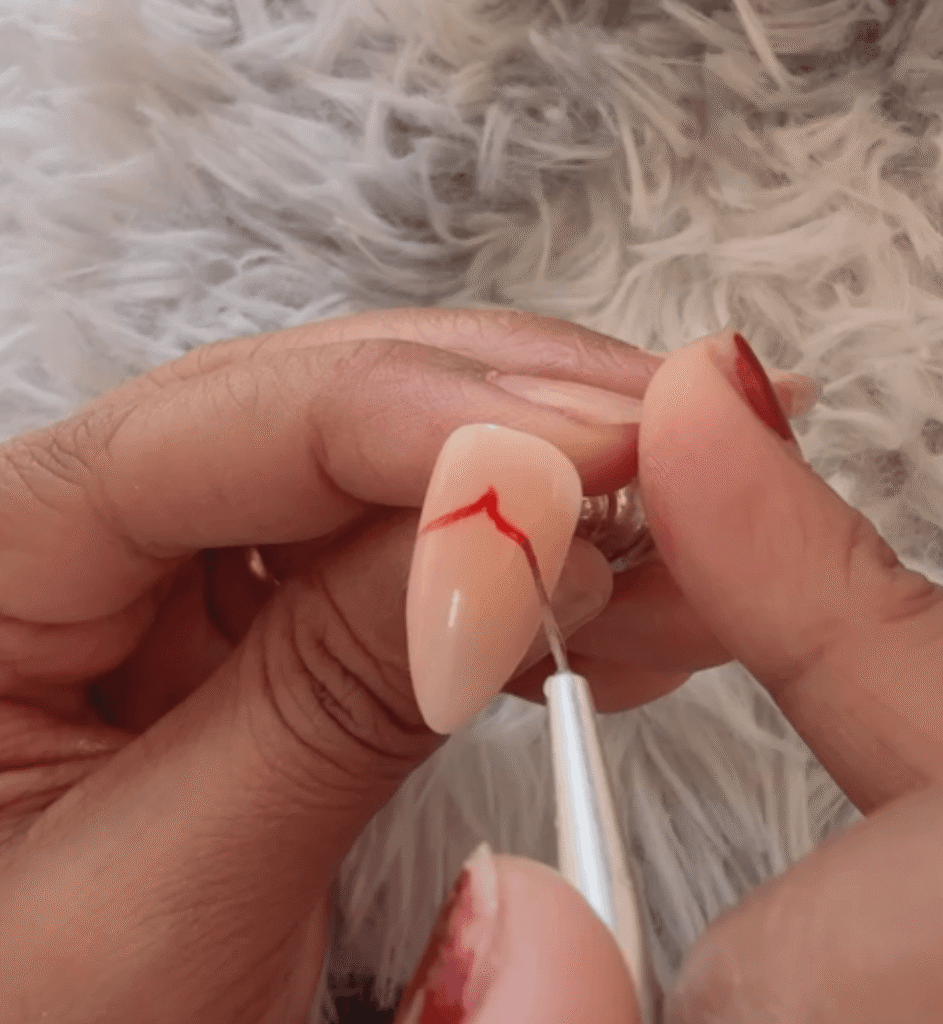 Close up of a nail technician using a fine liner brush to paint the curved red dome of an umbrella on a gel nail.