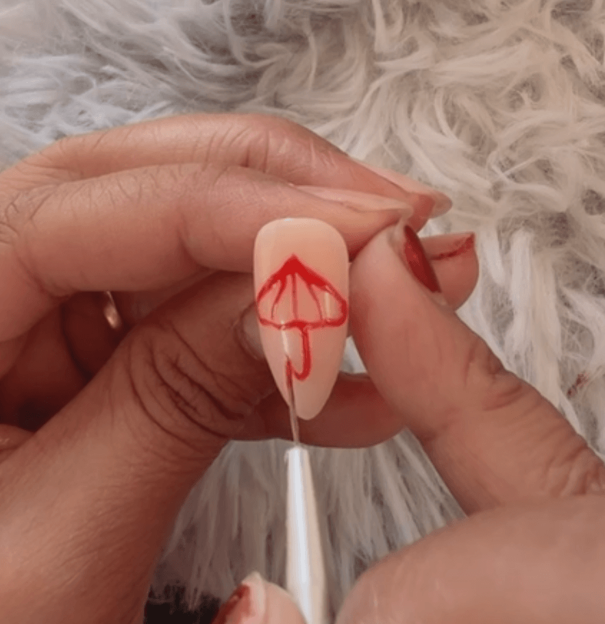 Using a fine detail brush to paint the curved bottom hook of a red umbrella nail design.