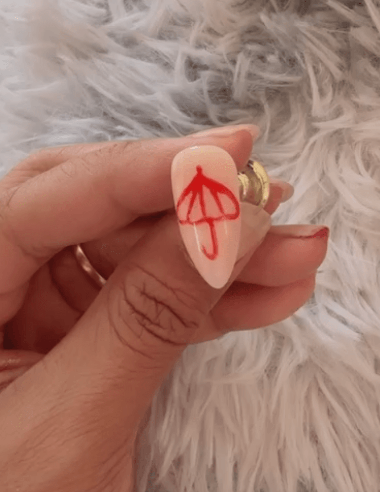 Completed freehand red umbrella nail art design on a translucent nude jelly gel base, shown on an almond shaped nail.